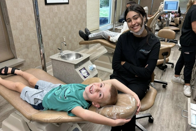 Patient receiving dental examination on chair in orthodontic office with staff member present.