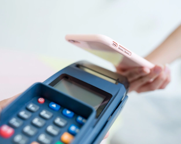 Hand holding credit card over blue payment terminal for contactless transaction.