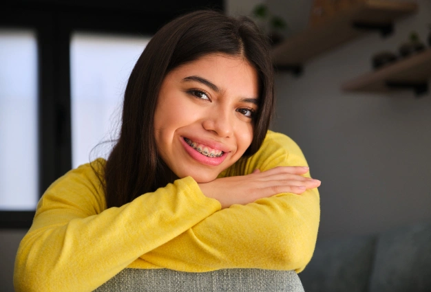 Smiling woman in yellow sweater leaning on gray couch in home setting.