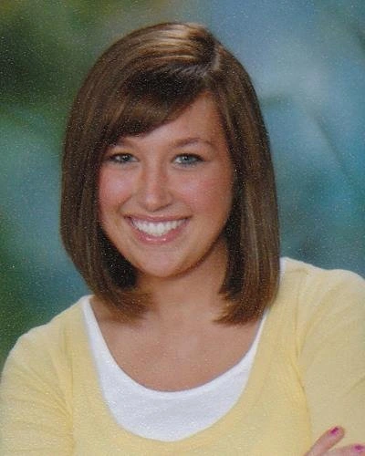 Young woman smiling at camera wearing yellow cardigan over white shirt, professional portrait style photo.