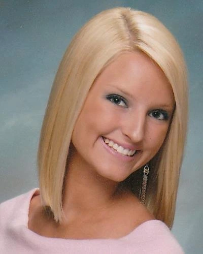 Young woman with blonde hair smiling at camera in professional portrait setting.