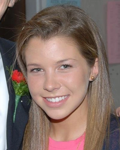 Young woman smiling at camera wearing pink top with flower accessory in hair