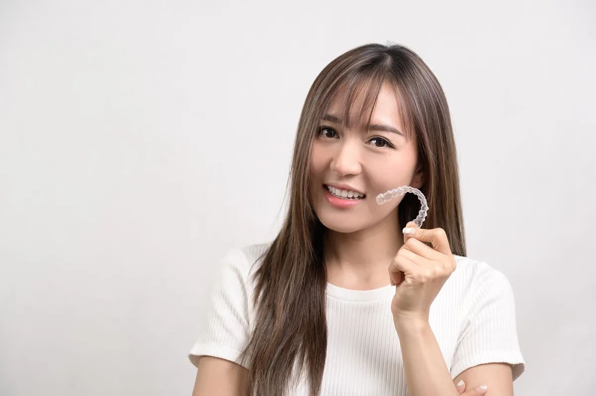 smiling woman holding invisalign clear aligner