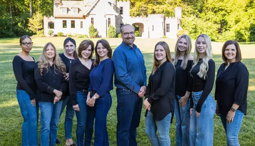 Dental practice team of ten professionals posing together on lawn in front of white building in Mayfield, Ohio.